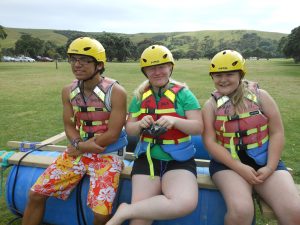 Three young people wearing helmets prepare to go rafting